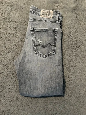 Grå jeans från Replay - Snygga grå jeans från Replay med slitningar och klassisk femficksdesign. Jeansen har en cool tvättad look, detaljerad bakficka med broderad våg och Replay-märke på linningen. Perfekta för en avslappnad och trendig stil. Lappen för storlek är tyvärr bortklippt så SE MÅTT!