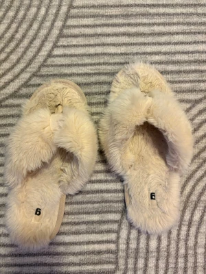 Beiga fluffiga tofflor med korsad rem - Supermjuka och fluffiga tofflor i beige färg från ginatricot med korsade remmar över foten. Sula i samma mjuka material för extra komfort. Storlek EU ungefär 38-40