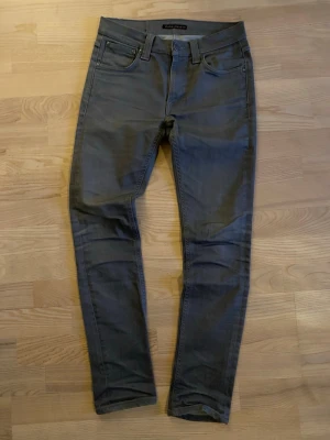 Grå slim fit Nudie Jeans - Snygga grå slim fit jeans från Nudie med klassisk femficksdesign och bälteshällor. Jeansen har raka ben och diskreta sömmar, perfekta för en stilren look. Materialet är mjukt och stretchigt för extra komfort. |W28 L32| Modellen Lean Dean! Hör av er vid minsta fundering, kan sänka priset vid snabb affär!