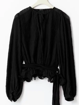 Svart långärmad blus med knytband - Trendig svart blus från Gina Tricot med långärmade, lätt puffade ärmar och knytband i midjan. Blusen har en v-ringning med dekorativt band och volangdetaljer vid nederkanten. Materialet är lätt och strukturerat för en cool look. Endast använd en gång 