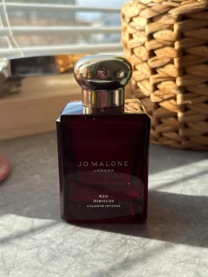 Jo Malone Red Hibiscus parfym - En elegant parfym från Jo Malone i doften Red Hibiscus. Flaskan är mörkröd och fyrkantig med en blank, silverfärgad rund kork. Designen är stilren och lyxig, perfekt för dig som gillar exklusiva dofter och snygga flaskor i badrumshyllan. 50ml endast testad 