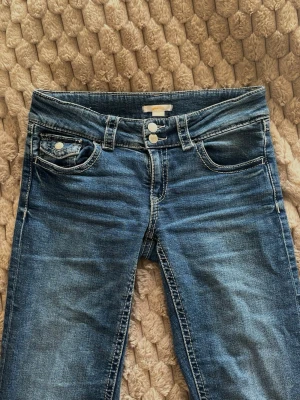 Blå Bootcut Jeans - Gina Tricot - Snygga blå bootcut jeans från Gina Tricot med klassisk femficksdesign, dubbla silverknappar och tydliga sömmar. Jeansen är mellan lowwaist och midwaist. Storlek 170/S/XS (ungefär). Fin modell och fin färg. Små slitningar.