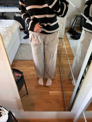 Beiga vida linnebyxor med dragsko - Säljer ett par beiga linnebyxor med avslappnad passform och dragsko i midjan. Byxorna har raka, vida ben och är tillverkade i ett lätt och luftigt linnematerial. Perfekta för en chill och stilren look.