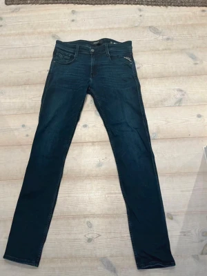 Mörkblå slim fit jeans från Replay - Snygga mörkblå slim fit jeans från Replay med klassisk femficksdesign och läderpatch bak i midjan. Jeansen har smal passform och är tillverkade i ett stretchigt denimtyg som sitter skönt hela dagen. Perfekta till en avslappnad streetstyle-look.