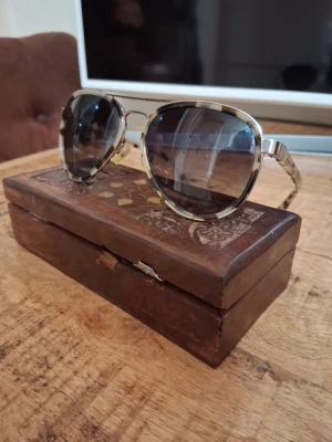 Solglasögon Taylor Morris  - Snygga solglasögon med rundad form och transparent beige båge med leopardmönster. Glasen är mörka och ger en cool retrovibe. Perfekta för att lyfta din stil under soliga dagar.