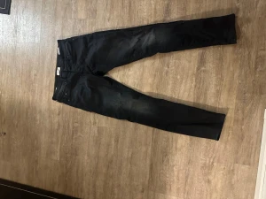 Svarta slim fit jeans från Jack & Jones - Snygga svarta slim fit jeans från Jack & Jones med klassisk femficksdesign och orangea kontrastsömmar. Jeansen har en smal passform och är tillverkade i stretchigt denimtyg för extra komfort. Perfekta för en trendig och avslappnad stil.