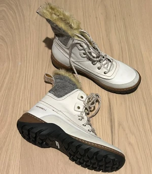 Vita vinterkängor från Merrell - Snygga vita kängor från Merrell med grå stickad skaft och beige fuskpäls upptill. Grov sula för bra grepp och snörning framtill. Perfekta för kalla dagar och outdoor-äventyr. Sköna och varma med cool design.