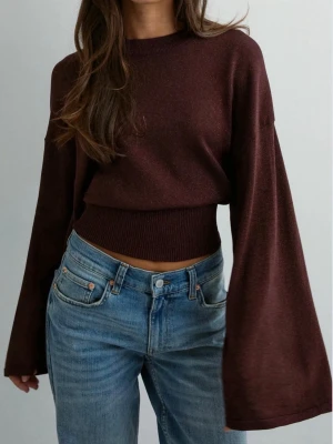 Brun/vinröd croppad tröja med vida ärmar - Säljer en mörkbrun/vinröd croppad tröja med bred ribbad midja och extra vida ärmar. Är också lite glittrig. Tröjan har rund halsringning och är tillverkad i ett mjukt, stretchigt material. Perfekt för dig som gillar en trendig och avslappnad stil.