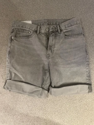 Grå jeansshorts - Snygga grå jeansshorts med klassisk femficksdesign och upprullad kant nedtill. Perfekta för en avslappnad stil och passar till det mesta. Gjorda i mjuk bomull med en normal passform och midwaist. Oanvända.