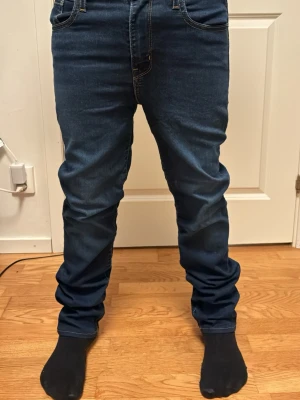 Mörkblå jeans från Levi's - Säljer ett par mörkblå jeans från Levi's med klassisk femficksdesign och raka ben. Jeansen har kontrastsömmar och en liten röd Levi's-tag på bakfickan. Tillverkade i slitstark denim med snygg passform som funkar till det mesta.