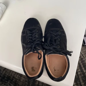 Christian Louboutin sneakers svart - Snygga svarta sneakers med den ikoniska röda sulan från Christian Louboutin. Skorna har snörning och en stilren design som passar perfekt för en trendig look.