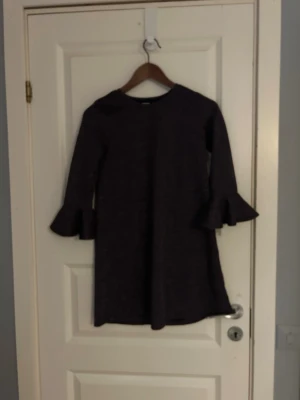 Glittrig svart klänning - Snygg svart glittrig klänning från Lindex med långärmade trumpetärmar. Klänningen har en rak passform och är tillverkad i ett glittrigt syntetmaterial som ger en cool look. Perfekt för dig som gillar att sticka ut med lite extra glitter. Perfekt för nyår eller fest.