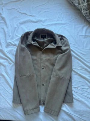 Beige overshirt från Jack n jones - Stilren beige overshirt från Jack n Jones i ett mjukt, lite tjockare bomullstyg. Rak passform med klassisk krage, tryckknappar framtill och diskreta sidofickor. Perfekt lager-på-lager-plagg för en clean look.