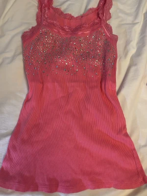 Rosa spets linne med glitter - Supersöt rosa linnetopp med ribbad struktur, spetsdetaljer vid axelbanden och massor av glittrande. Den är thriftad på vintage marknad utomlands! 