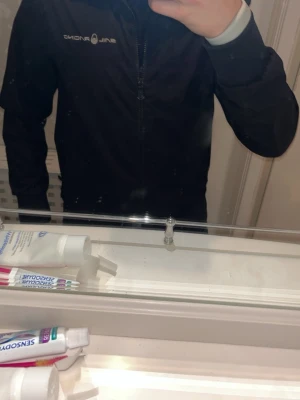 Svart vindjacka från Sail Racing - Snygg svart vindjacka från Sail Racing med dragkedja framtill och diskret logga på bröstet. Jackan har en minimalistisk design och är tillverkad i ett lätt och vindtätt material, perfekt för blåsiga dagar. Passar dig som gillar stilrena och sportiga plagg. Nypris 2000kr. Några små fläckar med blå färg inuti. Storlek small men passar även m. Pris kan diskuteras och öppen för byten 