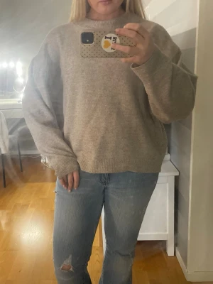 Beige oversized stickad tröja - Mysig beige stickad tröja med rund hals och avslappnad, oversized passform. Tröjan har ribbade muddar vid ärmslut och nederkant. Perfekt för lager på lager och enkel att matcha med jeans eller kjol.