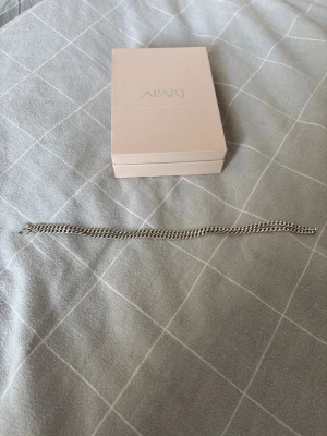Silverfärgat kedjehalsband från Apart - Silver halsband från apart fick den av mitt ex så vill bara bli av med den. Halsbandet är 55cm långt bra kvalité men bör tvättas ifall ni vill ha den mer glansig, duschat och badat med den så kan garantera att halsbandet är äkta🙂 ifall ni har mer frågor eller funderingar bara skicka MVH Emil. ❗️priset kan diskuteras❗️(boxen ingår)