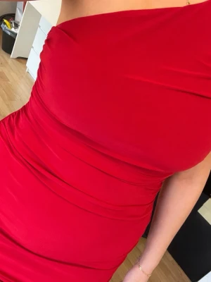 Röd oneshoulder klänning - Snygg röd klänning från Club London, med oneshoulder-design och draperad effekt. Klänningen har en tight passform och är tillverkad i ett mjukt, stretchigt material som sitter bekvämt mot kroppen. Går över knäna. Storlek 42.
