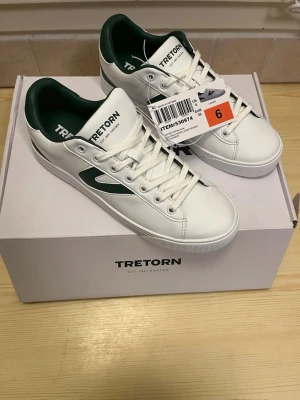 Vita och gröna sneakers från Tretorn strl 39 - Helt nya vita sneakers från Tretorn med gröna detaljer och logga på sidan och hälen. Skorna har snörning och en platt sula. Storlek 39. Aldrig använda och kommer i originalförpackning.
