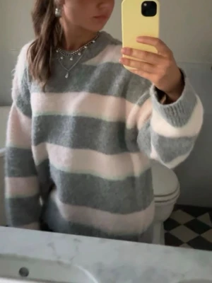 Randig oversized stickad tröja - Mysig stickad tröja med breda horisontella ränder i ljusgrått, ljusrosa och turkos. Tröjan har en oversized passform, långa ärmar och rund halsringning. Perfekt för dig som gillar en avslappnad och trendig stil. Storlek är L för att jag gillar att jag velat ha den overzised. Skriv för fler bilder❤️