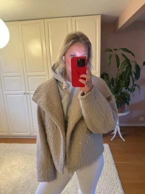 Vår jacka - Mysig och trendig teddyjacka i beige med bred krage och avslappnad passform. Jackan har en fluffig struktur och är perfekt för att hålla sig varm under kyliga dagar. Passar bra över en hoodie för en cool och avslappnad look.