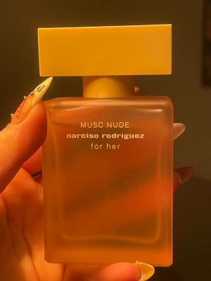 Musc Nude parfym från Narciso Rodriguez 50ml - Musc Nude från Narciso Rodriguez for her är en parfym i en matt, fyrkantig glasflaska med mjuk persikofärgad ton och matchande lock. Flaskan har en stilren och modern design med vit text på framsidan. Perfekt för dig som gillar eleganta och minimalistiska doftflaskor.