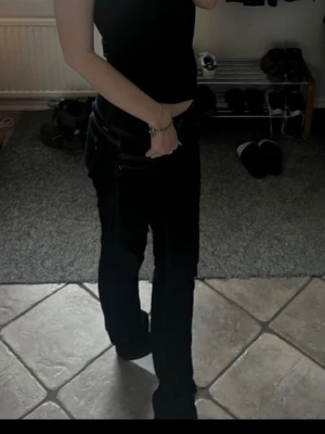 Mörkblå bootcut jeans med dubbla knappar - Säljer ett par mörkblå bootcut jeans med dubbla knappar i midjan och kontrastsömmar. Jeansen har låg midja och klassisk femficksdesign. Materialet är denim i bomull med lite stretch för skön passform. Perfekta för en trendig och avslappnad look.