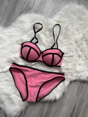 Rosa bikini med svarta kanter - Snygg bikini i rosa med svarta kontrastkanter och bygel-bh. Bikinin har justerbara axelband och klassisk trosa. Perfekt för strand eller poolhäng och ger en sportig men trendig look.
