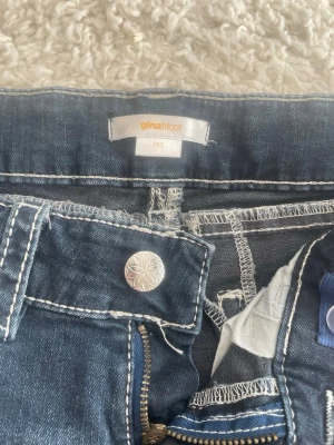 Blå jeans med paljettficka Gina Tricot - Snygga lågmidjade blå jeans från Gina Tricot med dekorativ bakficka prydd med paljetter och broderi. Jeansen har kontrastsömmar, klassisk knapp och dragkedja framtill. Perfekta för dig som vill sticka ut lite extra med detaljer. Använt några gånger inga fläckar eller märken!