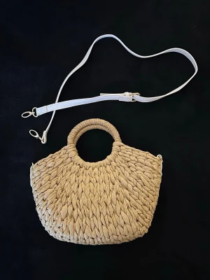 Beige flätad beachväska från ASOS med axelrem - Superfin beige flätad väska från ASOS Design. Perfekt till strand, beachclub och semester.  Kan bäras i handtaget eller med den avtagbara vita axelremmen (crossbody).  Fint skick. Rymmer mobil, plånbok, solkräm och småsaker.