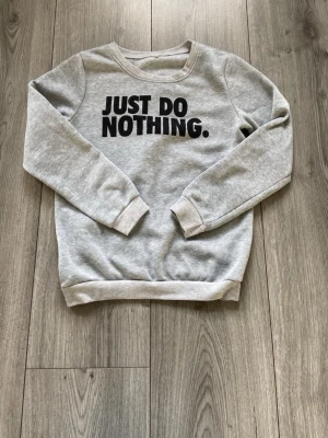 Grå sweatshirt med tryck - Grå sweatshirt med svart text 'JUST DO NOTHING.' på bröstet. Tröjan har rund hals, långa ärmar och ribbade muddar vid ärmslut och nederkant. Perfekt för en avslappnad stil och gjord i mjukt material.