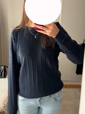 Mörkblå kabelstickad tröja - Mörkblå kabelstickad tröja med rund halsringning och långa ärmar. Tröjan har klassiskt flätmönster och ribbade muddar vid ärmslut och nederkant. 