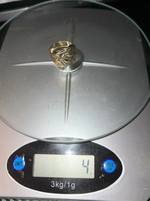 Versace ring 14 karat guld  - Unik guldfärgad ring i metall med fyrkantig front, dekorerad med ett detaljerat öga och vingar på sidorna. Ringen har en bred design och coolt motiv som sticker ut. Perfekt för dig som gillar smycken med symbolik och attityd.