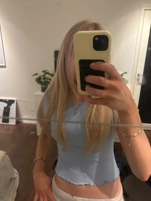 Ljusblå croppad ribbad topp - Säljer en ljusblå croppad topp med korta ärmar och ribbad struktur. Toppen har vågig kant nertill och vid ärmslut, vilket ger en söt och trendig look. Perfekt för dig som gillar en enkel men stilren stil.