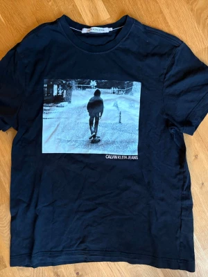 Svart Calvin Klein Jeans t-shirt - Svart t-shirt från Calvin Klein Jeans med tryck av en skateboardåkare på framsidan och liten logga i nacken. Klassisk rund hals och korta ärmar. Skön bomullskvalitet som passar perfekt till jeans eller shorts.
