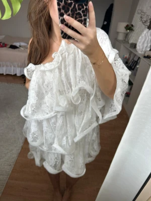 Vit spetsklänning med volanger - Supersöt klänning i spets med flera lager volanger och en axelbandslös design. Lojsans kollektion med NAKD