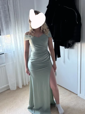 Ljusgrön offshoulder långklänning - Snygg ljusgrön långklänning med offshoulder-design. Klänningen har en figurnära passform och är perfekt för speciella tillfällen. Den ha även en slits på sidan. Skriv gärna om du vill ha fler bilder på klänningen.
