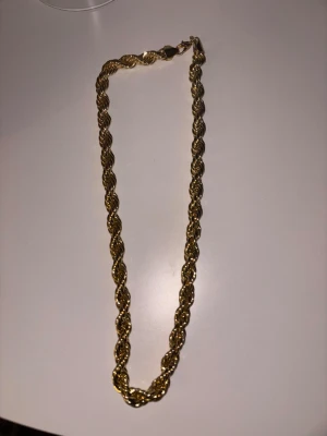 Cordell halsband (Guld 10mm 60cm) - Säljer ett snyggt halsband med repkedja i guldfärg. Halsbandet har en tvinnad design som ger ett maffigt intryck och stängs med ett klassiskt lås. Perfekt för dig som vill ha ett statement-smycke som sticker ut.