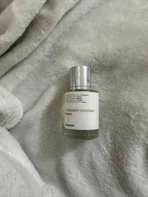Powdery Coconut parfym från Dossier - Fräsch och modern parfym från Dossier med doften Powdery Coconut. Flaskan är genomskinlig med en stilren vit etikett och ett silverfärgat lock. Perfekt för dig som gillar kokos och vill ha en enkel men snygg parfymflaska i badrumsskåpet.