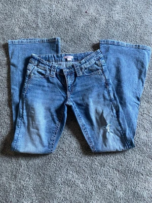 Blå bootcut jeans med slitning - Säljer ett par blå bootcut jeans med cool slitning på benen. Perfekta för dig som gillar en avslappnad och trendig stil.