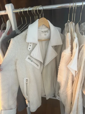 Vit teddyjacka  - Säljer en snygg vit teddyjacka från med dragkedja och detaljer i vitt konstläder. Jackan har fickor med dragkedja och bälte vid ärmsluten. Perfekt för dig som vill ha en trendig och mysig look.