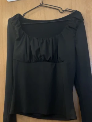 Svart långärmad topp med rynkad urringning - Trendig svart långärmad topp med bred, rynkad urringning och figurnära passform. Tillverkad i ett mjukt, stretchigt material som ger en bekväm känsla. 