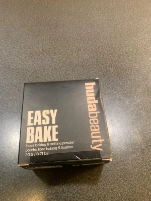 Huda Beauty Easy Bake Blondie puder - Huda Beauty Easy Bake Loose Baking & Setting Powder i nyansen Blondie. Puder i en fyrkantig plastburk med svart lock, perfekt för att fixera sminket och ge en matt finish. Färgen är ljusbeige och passar dig som vill ha en naturlig look.
