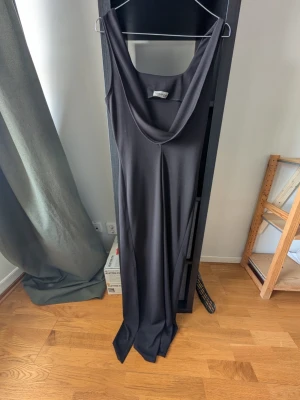 Svart långklänning från Terranova - Säljer en svart långklänning från Terranova med snygg draperad ringning. Klänningen har ärmlös design och ett elegant, minimalistiskt uttryck. Perfekt för dig som gillar stilrena plagg med en modern twist.