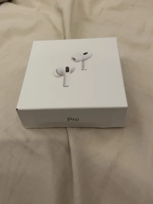 Apple AirPods Pro trådlösa hörlurar - Säljer ett par vita Apple AirPods Pro med laddningsetui. De är trådlösa in-ear-hörlurar med stilren design och kompakt format. Perfekta för musik, samtal och gaming. Levereras i originalförpackning med laddningscase i plast.