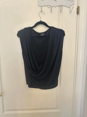 Svart draperad ärmlös topp/blus  - Snygg svart topp med draperad framsida och ärmlös design. Toppen är endast använd ett påtal gånger- alltså i bra skick. Toppen passar perfekt till fest eller när som! Hör av er vid funderingar!💗