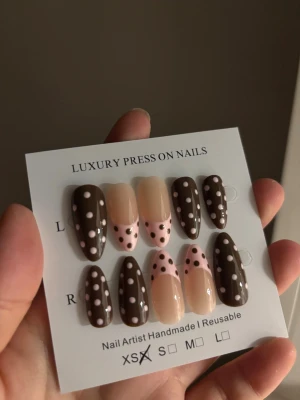 Bruna och rosa prickiga press-on naglar - Snygga press-on naglar i mandelform med brun bas och vita prickar samt nude och rosa fransk design med prickar. Handgjorda och återanvändbara, perfekta för dig som vill ha en trendig och lekfull look. Kommer i storlek XS.