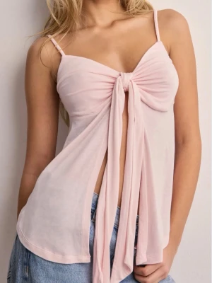 Ljusrosa omlottopp med knyt - Trendig ljusrosa topp med tunna axelband och stor knytning framtill som ger en omlott-effekt. Toppen är ärmlös och har en luftig, flowy passform som passar perfekt till jeans eller kjol. Materialet känns mjukt och lätt mot huden.