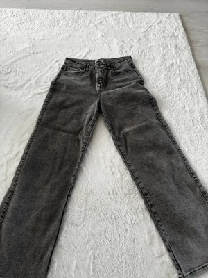 Grå raka jeans från Madlady - Säljer ett par grå jeans från Madlady i rak modell med hög midja. Jeansen har klassiska fem fickor, bälteshällor och stängs med knapp och dragkedja. Materialet är denim i en tvättad grå nyans som ger en cool vintagekänsla.