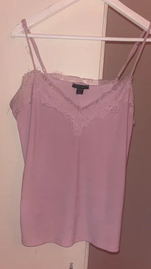 Ljusrosa linnetopp med spets - Söt ljusrosa linnetopp från MISU med tunna axelband och v-ringning dekorerad med spets. Toppen har en mjuk och följsam känsla, perfekt för att skapa en romantisk look. Enkel att matcha med både jeans och kjol. Liten fläck men inget som syns mycket. Liten fläck på men inget som syns mycket. Passar som M/S.